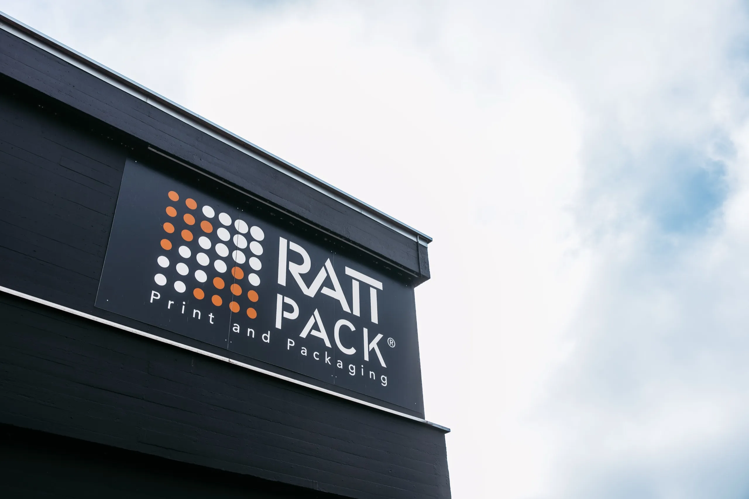 Fassade eines RATTPACK-Werks mit Firmenlogo vor bewölktem Himmel